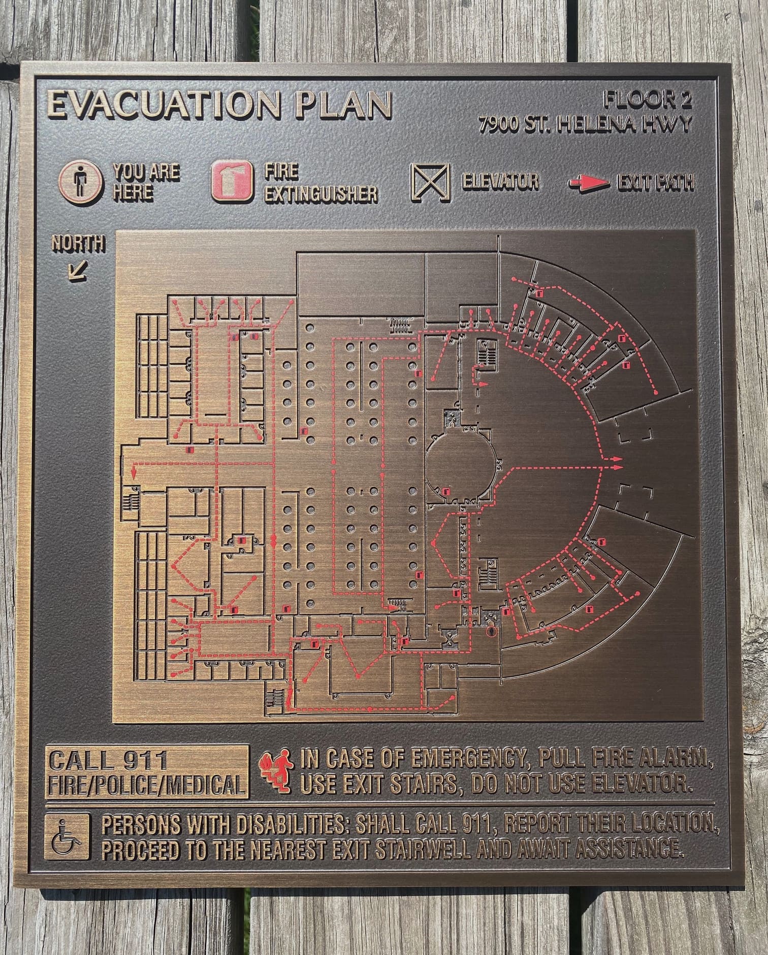 A bronze fire escape sign featuring a map of the area it is located within. Red lines on the map indicate proper escape routes in case of a fire.