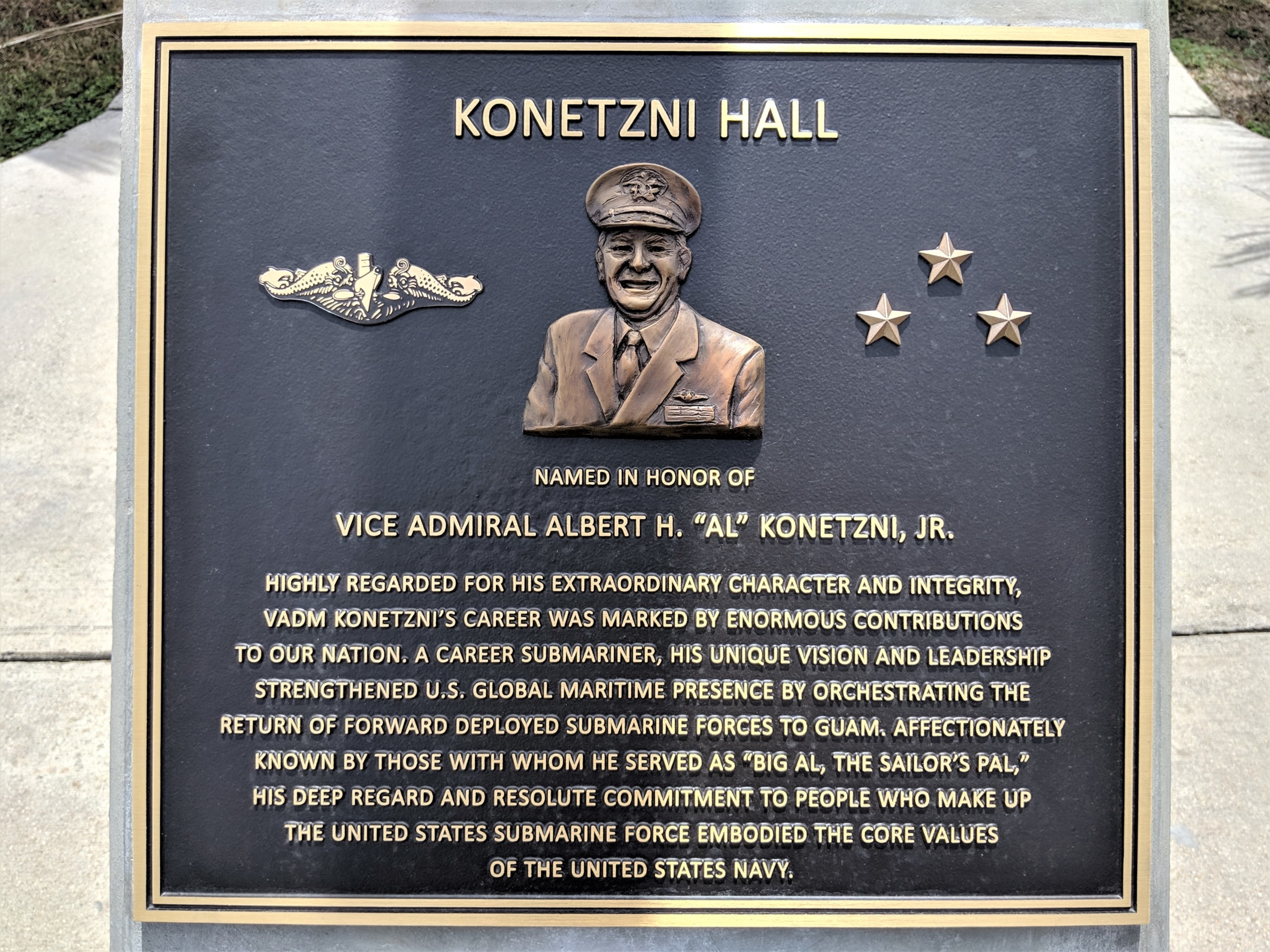 A bas relief cast bronze plaque in honor of U.S. Navy veteran Vice Admiral Albert H. Konetzni, Jr. A likeness of the Vice Admiral is present on the plaque.
