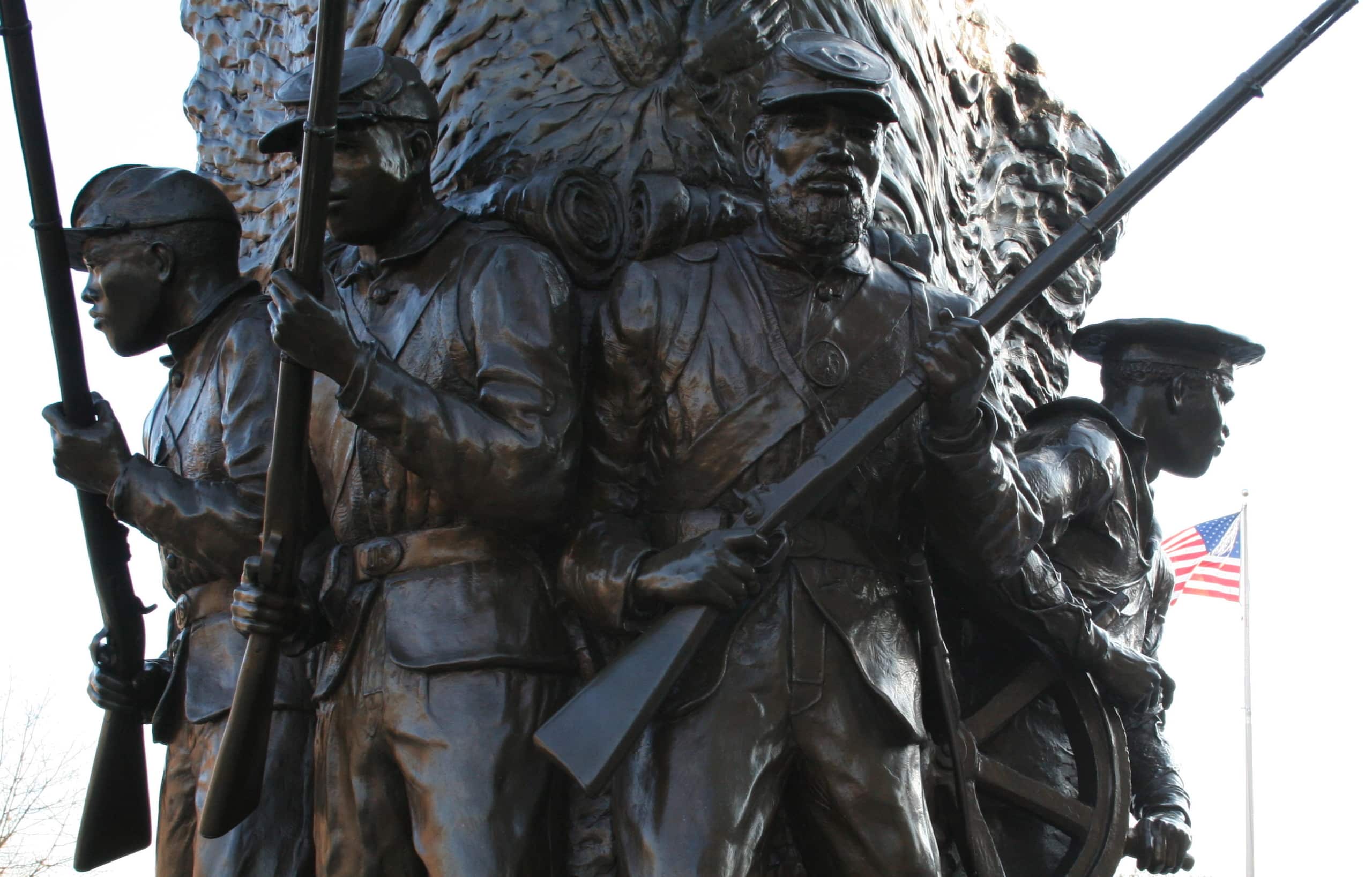 A close-up photograph of a bronze statue at the African American Civil War Memorial Museum. The veteran monument depicts four African American soldiers standing at the ready with muskets.
