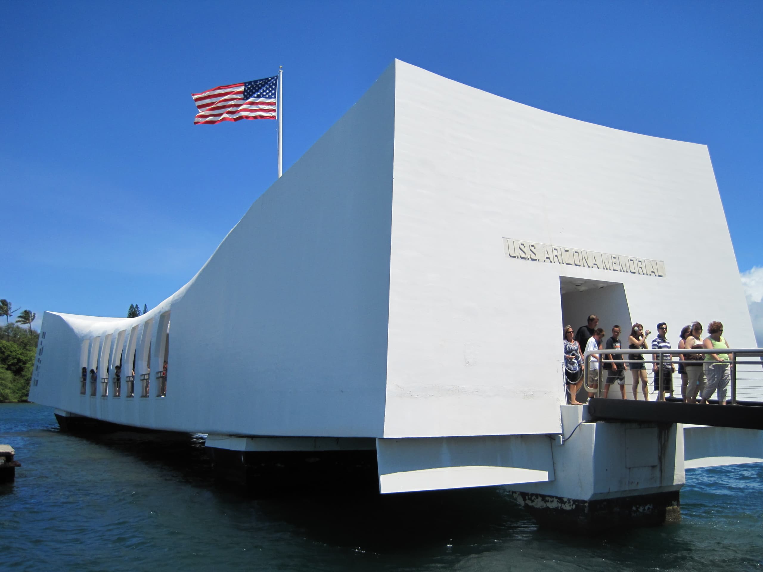 The USS Arizona Memorial contains a variety of plaques and other memorials preserving the attack on Pearl Harbor. Nine tourists are leaving the memorial.